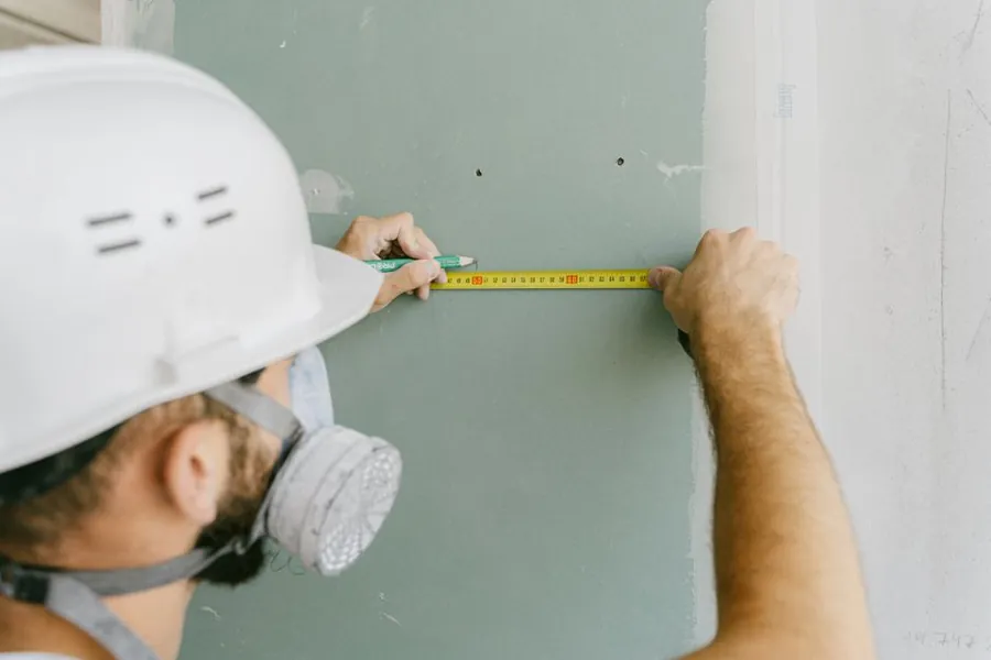 Builder measuring plasterboard during a garage annexe conversion, part of pricing the job accurately before work starts