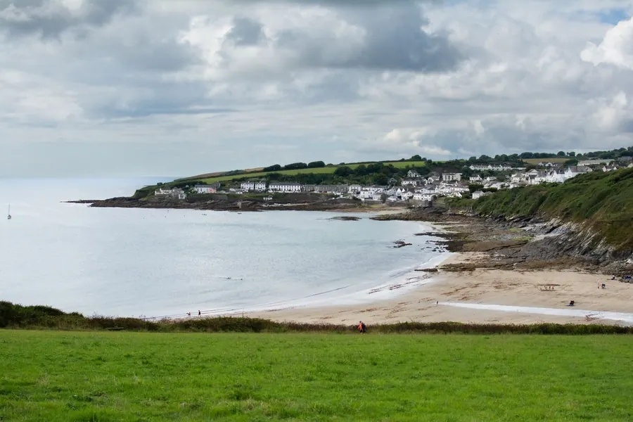 White houses strung along a headland above a sandy bay on the south Cornish coast, the kind of National Landscape setting where hip-to-gable loft conversions lose permitted development rights