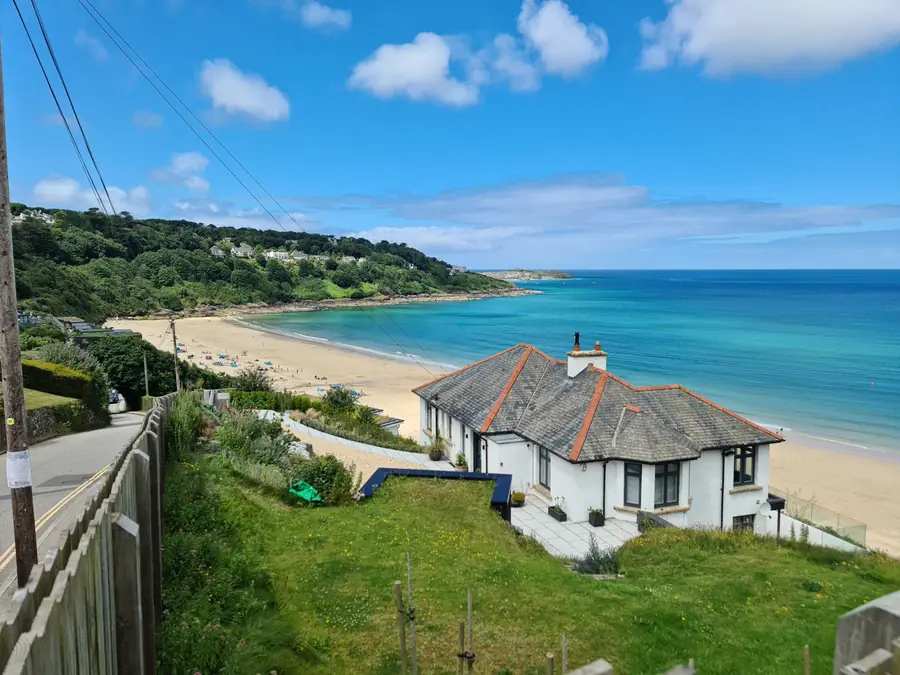 White rendered house with a hipped slate roof on a slope above a beach on the Cornish coast, showing how exposed a new gable wall would be to Atlantic weather