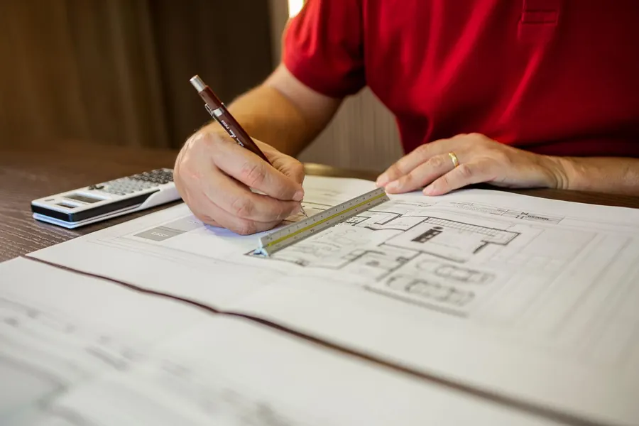 Hands drawing on a floor plan with a ruler and pen while a hip-to-gable loft conversion in Cornwall is measured up and priced