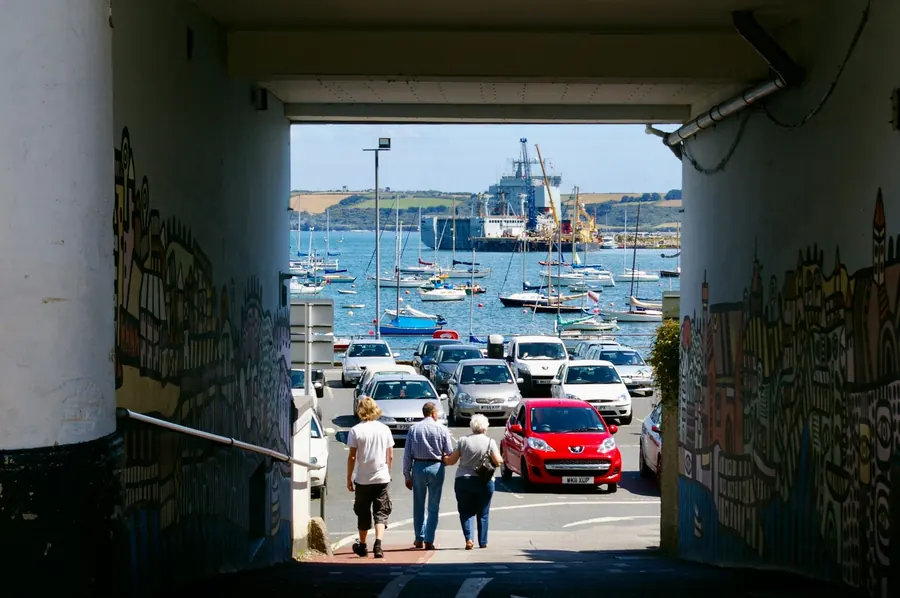 Narrow passage opening onto a packed waterfront car park with dock cranes beyond, showing how tight parking and access are for builders working on loft conversions in Falmouth
