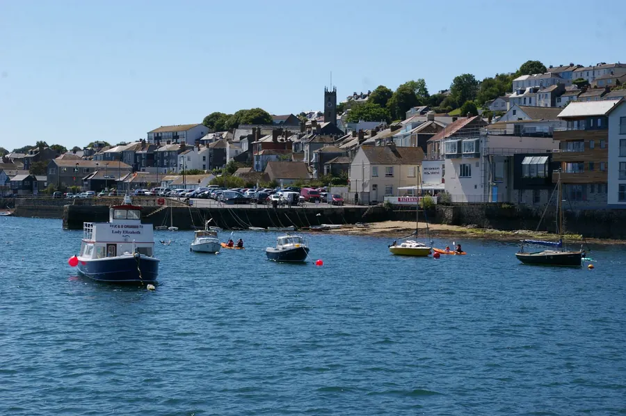 Houses and terraces stacked up a hillside above a harbour waterfront with moored boats, typical of the steep streets where loft conversions in Falmouth are built