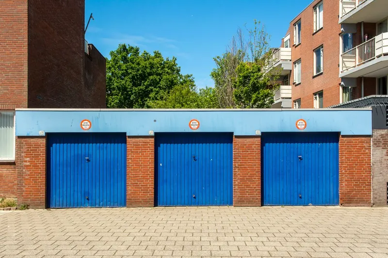 Block of sectional garages with painted metal doors behind housing, the garage-court arrangement common on older estates