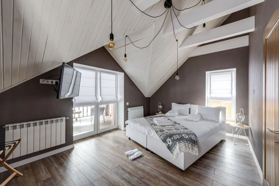 Finished attic bedroom with steeply sloping boarded ceilings and a dormer window, showing where the new structure of a converted trussed roof in Cornwall meets the usable headroom