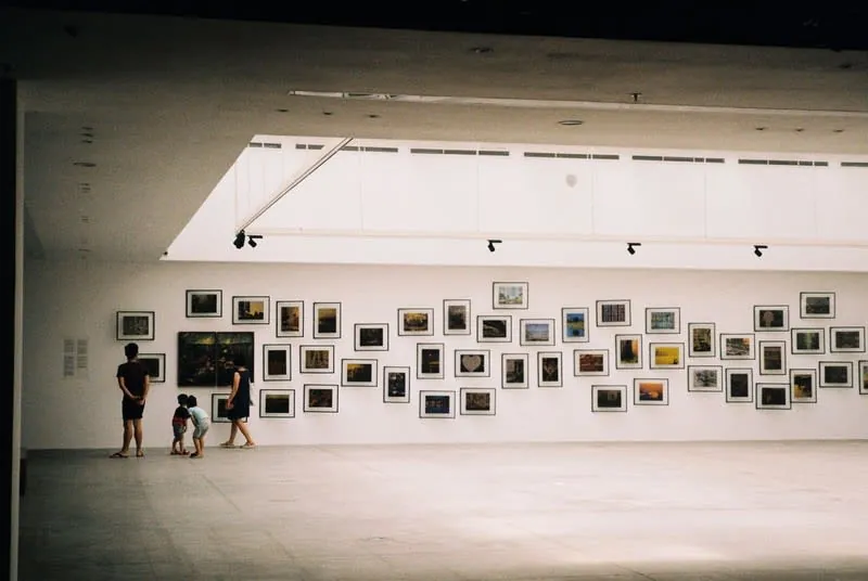 Visitors browsing a wall of framed works in a gallery exhibition