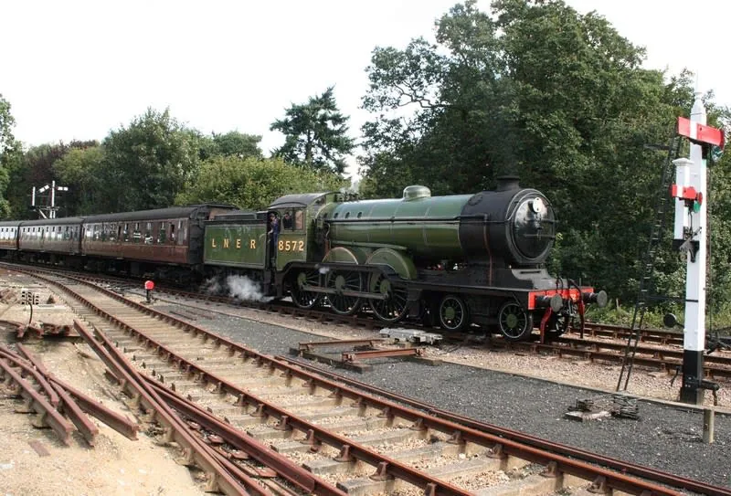 Green-liveried steam locomotive hauling carriages on a heritage railway line